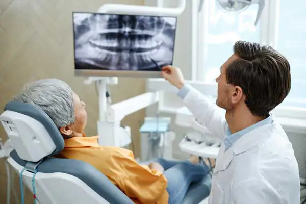 Back view of male dentist pointing at tooth X-ray image on screen during consultation at Riverwind Dental in Richmond, VA