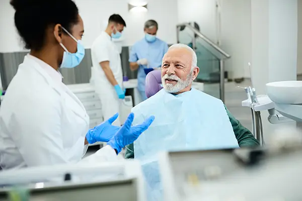 Older patient sitting in dental chair calmly discussing his oral health with his female dentist at Riverwind Dental in Richmond, VA