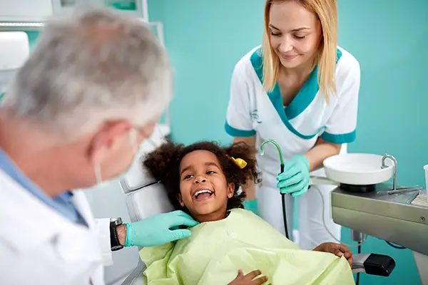 Adorable and young Black girl sitting in a dental chair and smiling at her dentist and assistant at Riverwind Dental in Richmond, VA