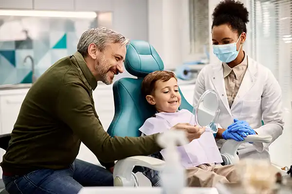Father holding a mirror for his happy, young son sitting in a dental chair at Riverwind Dental in Richmond, VA