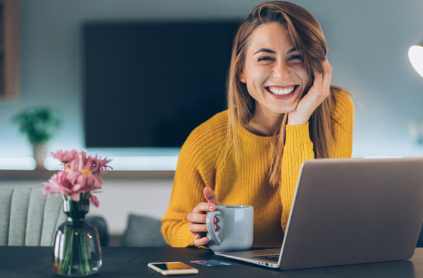 Woman smiling at desk with laptop after making her first visit to Riverwind Dental in Richmond, VA
