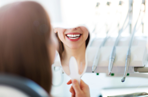 Woman looking at her restored smile in a mirror at Riverwind Dental in Richmond, VA