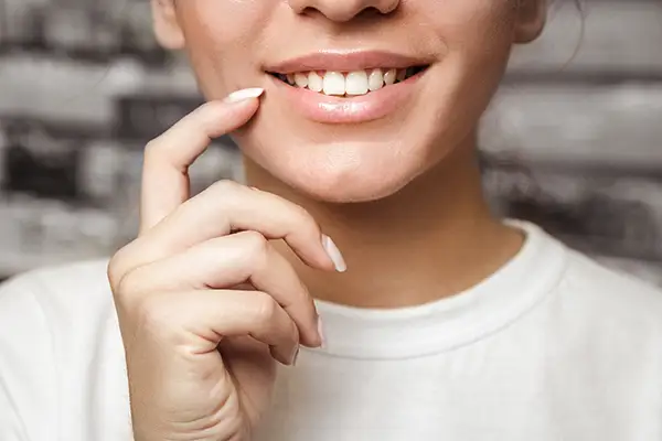 A close-up of a woman's smile as she gently touches her teeth with her finger after cosmetic dental treatment from Riverwind Dental in Henrico, VA