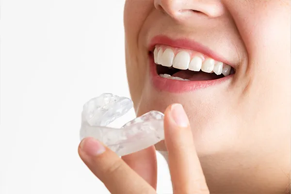 Close-up of a smiling woman holding a clear mouthguard near her teeth at Riverwind Dental in Richmond, VA