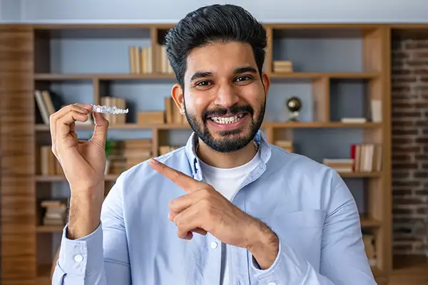 Smiling man holding and pointing at an Invisalign clear aligner at Riverwind Dental in Richmond, VA