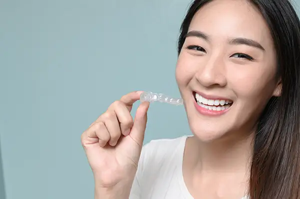 Young woman with a bright smile holding a Invisalign clear aligner at Riverwind Dental in Richmond, VA