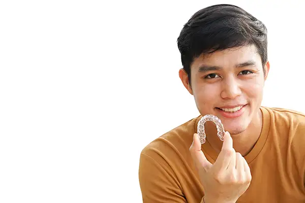 Smiling teenage boy holding a clear aligner in his hand, demonstrating its use as an alternative to traditional braces. Smiling teenage boy holding a clear aligner in his hand, demonstrating its use as an alternative to traditional braces.