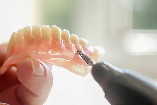 Close-up of a dental professional using a tool to adjust and customize a set of dentures for a patient at Riverwind Dental in Henrico, VA