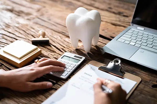 A man sitting at a desk with a calculator, laptop, and giant plastic tooth filling out insurance paperwork at Riverwind Dental in Henrico, VA